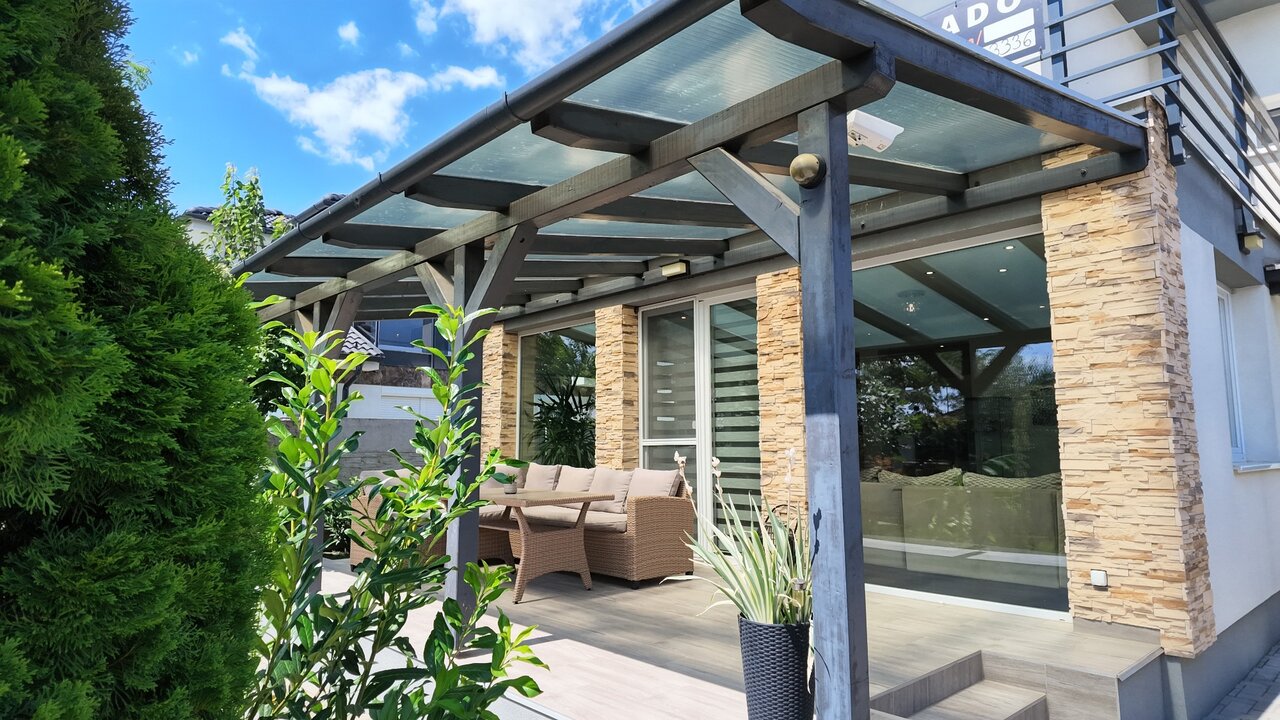 Pergola átlátszó tetővel a fedett terasz felett, kőburkolatos homlokzattal