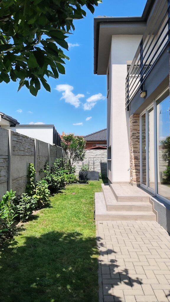 A családi ház modern homlokzata kőburkolattal, ápolt pázsittal és erkélykorláttal